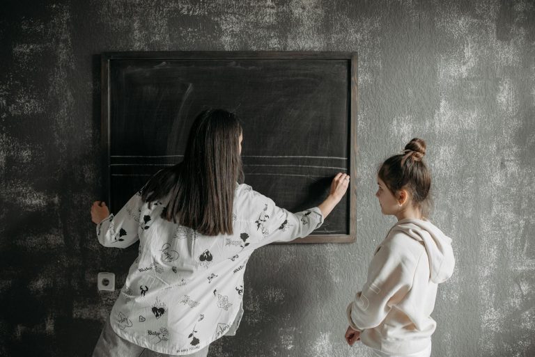 A teacher writing on a chalkboard during a private lesson with a child student indoors.